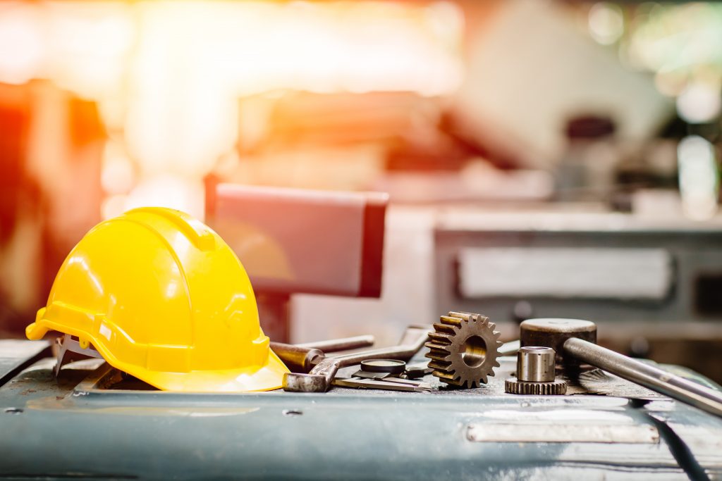 gele veiligheidshelm met gereedschap op een tafel met een machinefabriek op de achtergrond